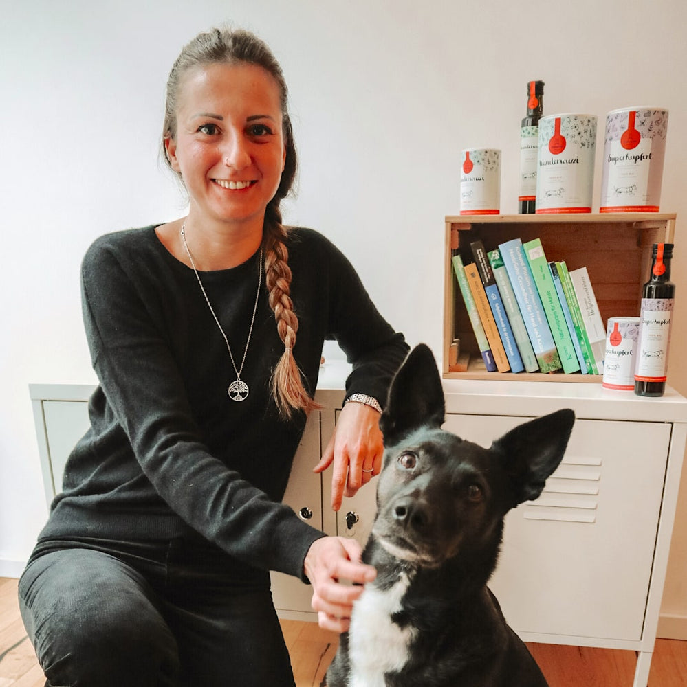 Hunde-Ernährungsexpertin Dani und Tierschutzhündin Tinka sitzen vor Fachliteratur zu natürlicher Hundeernährung, Tier-Naturheilkunde und Hundephysiotherapie.